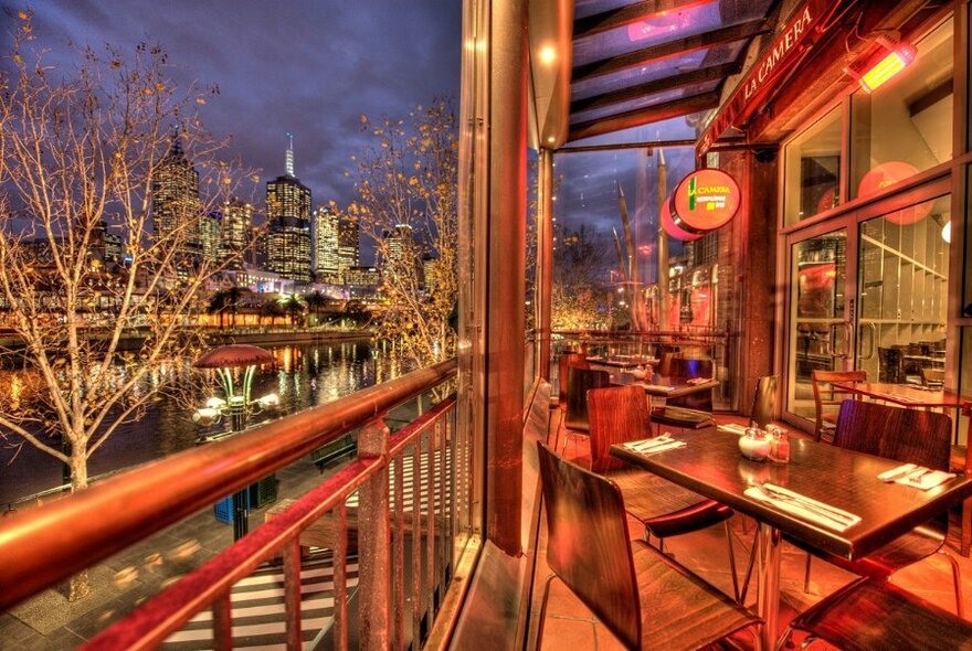 Terrace with set tables, bathed in red; river to left.