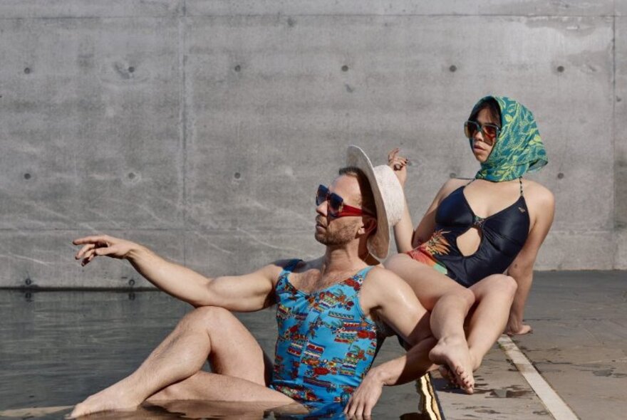 Two people in bathing costumes lounging in a concrete area.