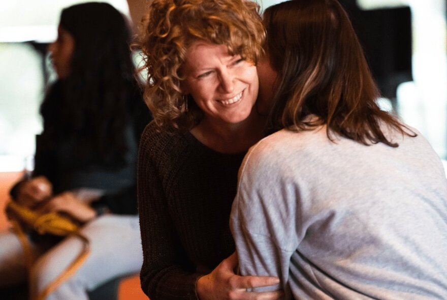 Two women hugging, one with her face visible and the other seen from behind.