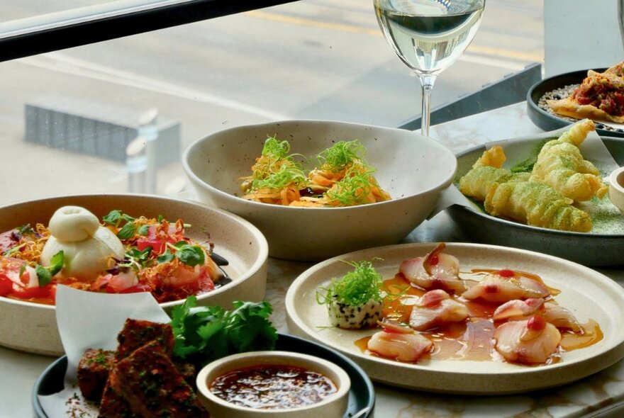 Plates of food on a restaurant table at Taxi Kitchen, with a glass of wine.