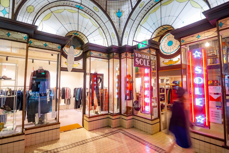 A person walking past two clothing shops in an art deco arcade.
