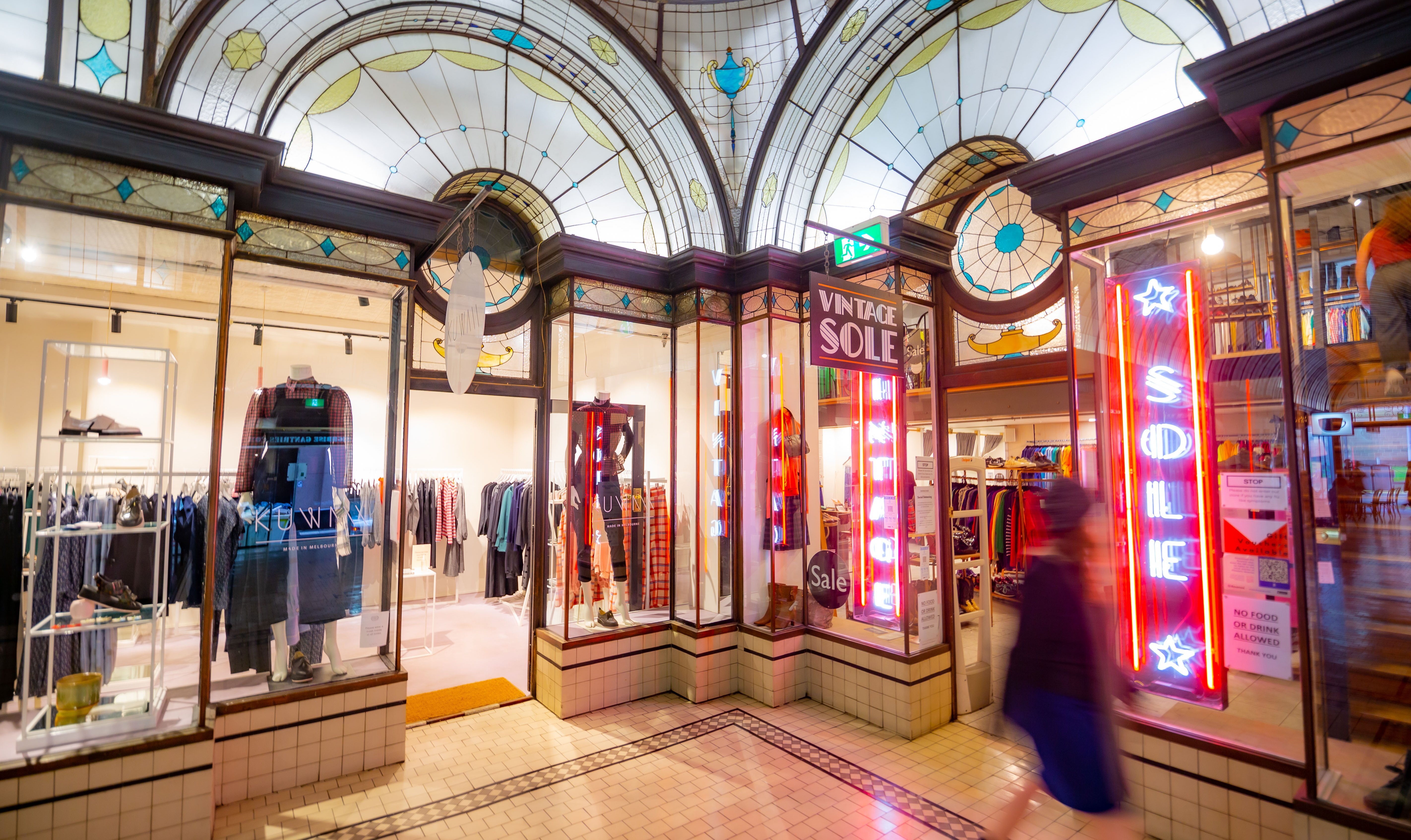 A person walking past two clothing shops in an art deco arcade.