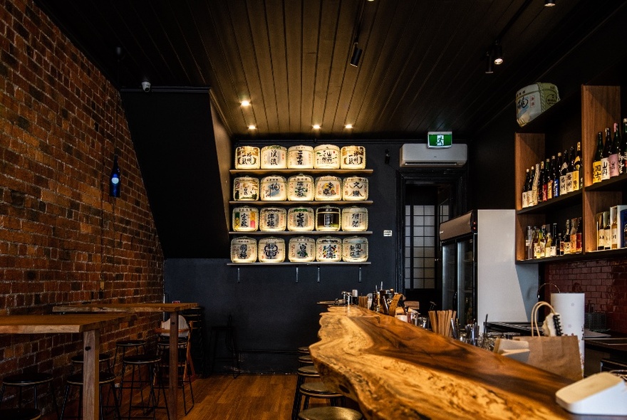 Interior of a Japanese sake bar with a rawedge timber bench and sake barrels on a shelf.