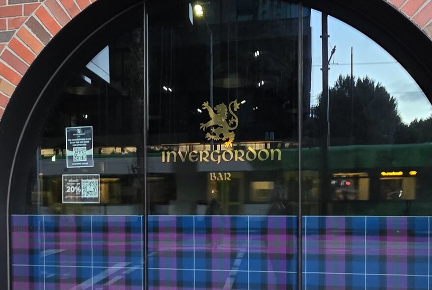 A close up of the arched window at Invergordon Bar, with the Invergordon logo and a Scottish tartan on the window.