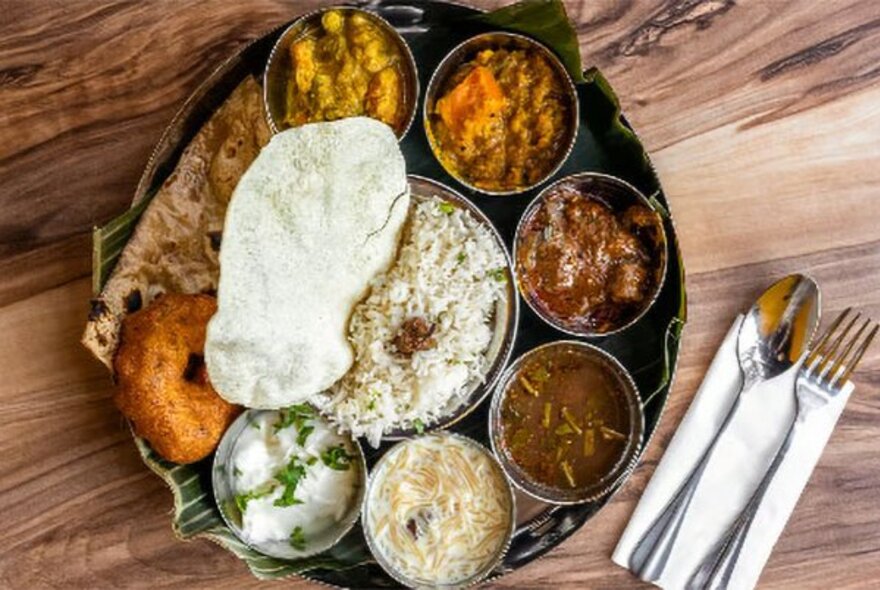 Thali Indian multicourse dish with rice, bread and raita, with cutlery.
