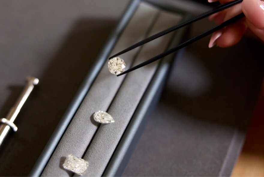 Loose diamonds showcased on a velvet display pad, with tweezers selecting one of the diamonds.