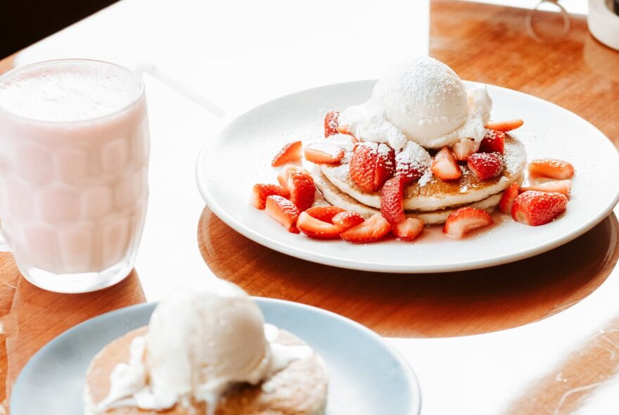 Looking down on a table on two plates of stacked pancakes, all with a scoop of ice cream and one with fresh strawberry toppings.