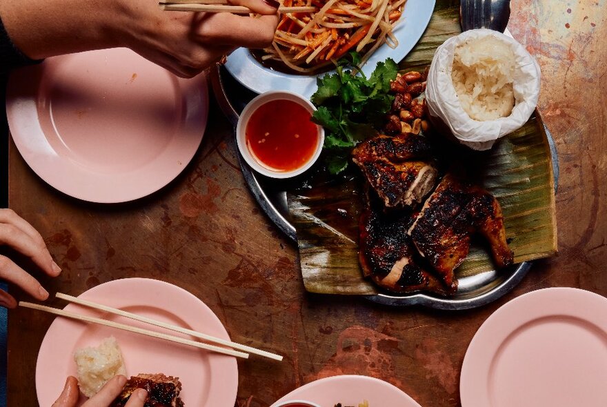 Four pink plates, one with chopsticks and a dumpling on it, surrounding an extravagant Thai-style dish. 