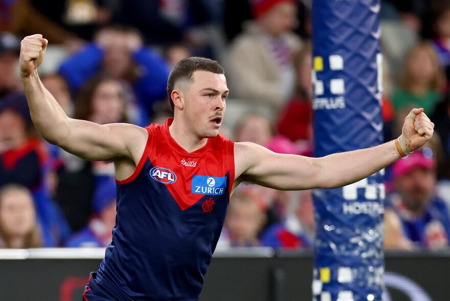 Melbourne AFL football player with arms outstretched during a match.
