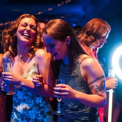A lively group of women laughing and dancing together under blue and ring-light illumination at an evening social event.