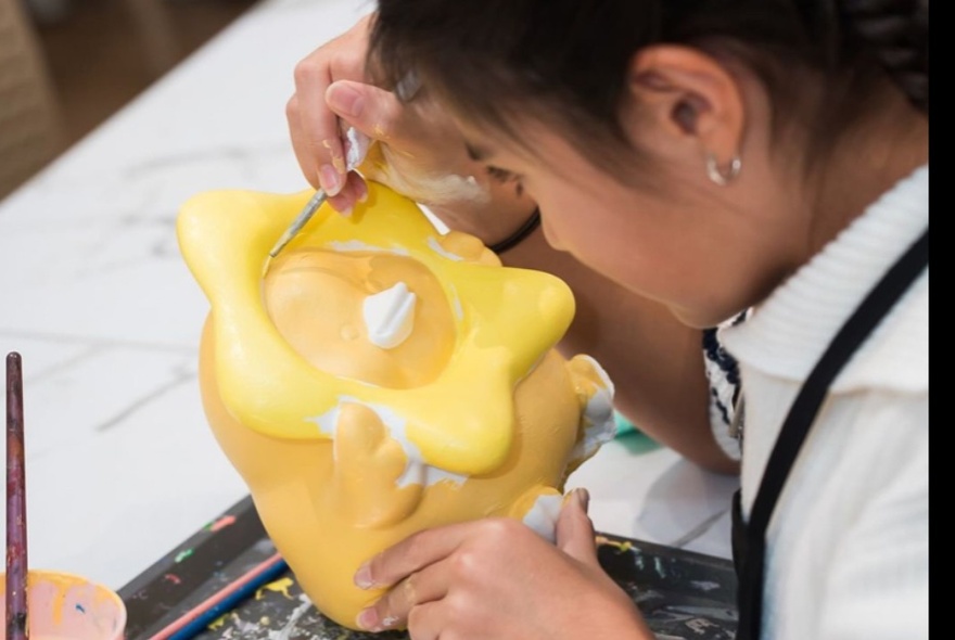 A young person concentrating and painting a plaster figurine.