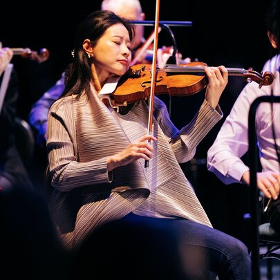 Violinists playing as part of a seated orchestra.