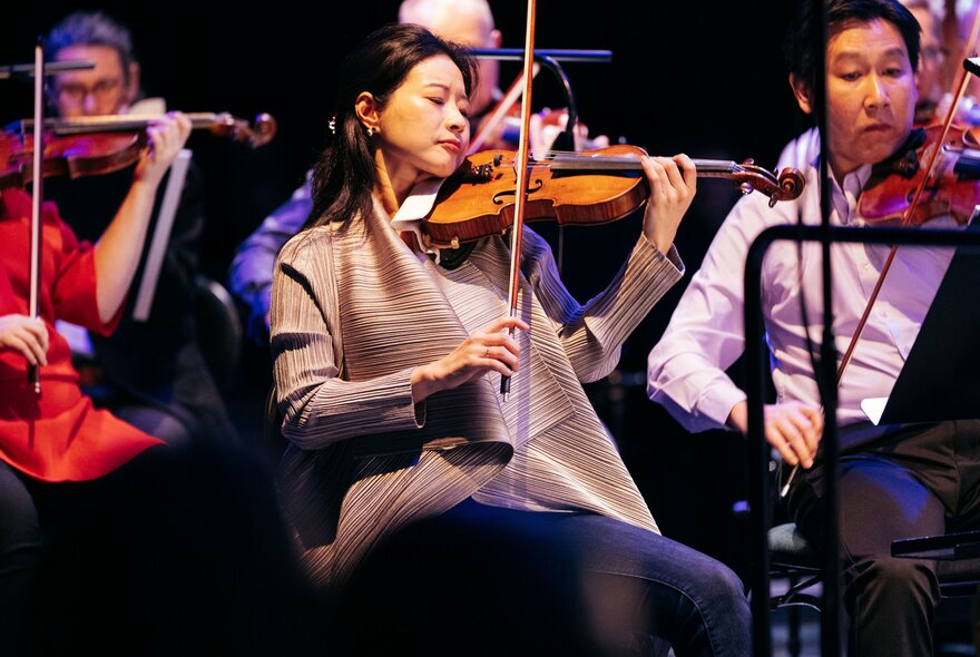 Violinists playing as part of a seated orchestra.