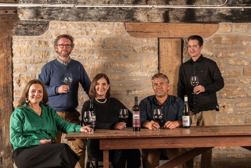 A group of winemakers and staff seated around a table, with bottles and glasses of wine, in a stone room at Wynns Coonawarra Estate. 