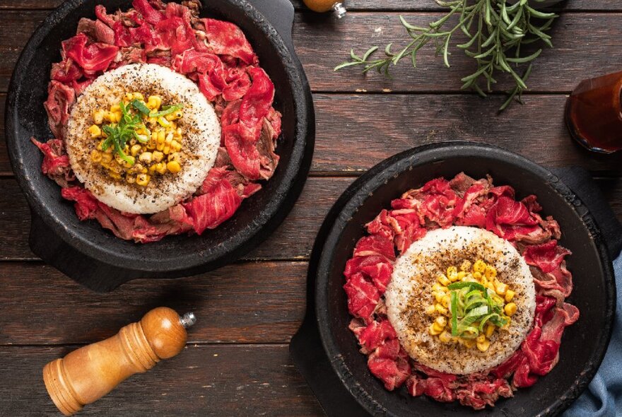 Bowls of faw meat topped with sauce and condiments on a wooden table.