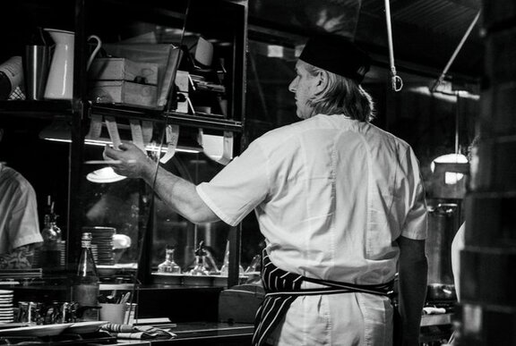 A chef in whites looking at kitchen dockets inside a commercial kitchen.