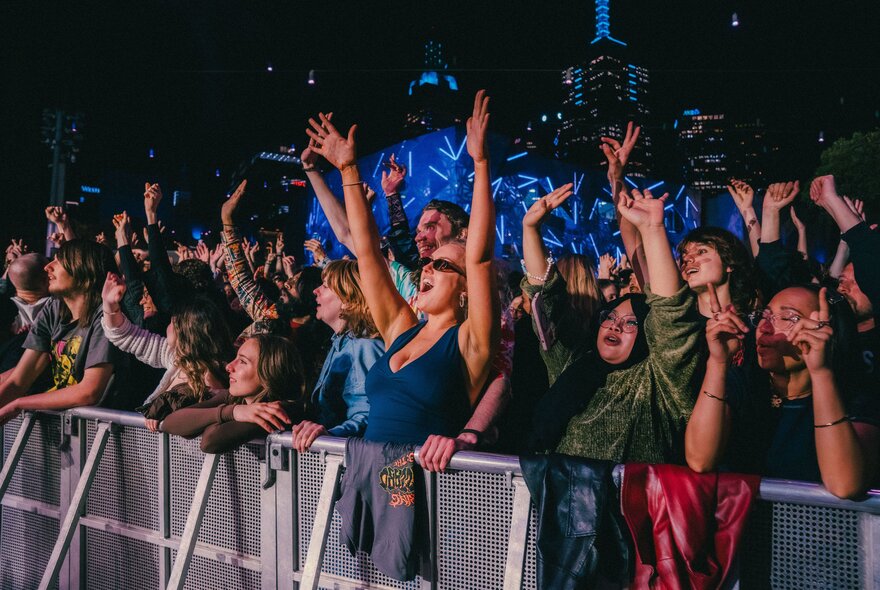 A live concert event at Fed Square at night, with a large, enthusiastic crowd gathered near a stage barrier.