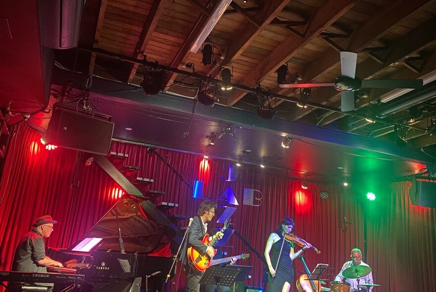 A musical band performing live on stage, red stage lights behind them.