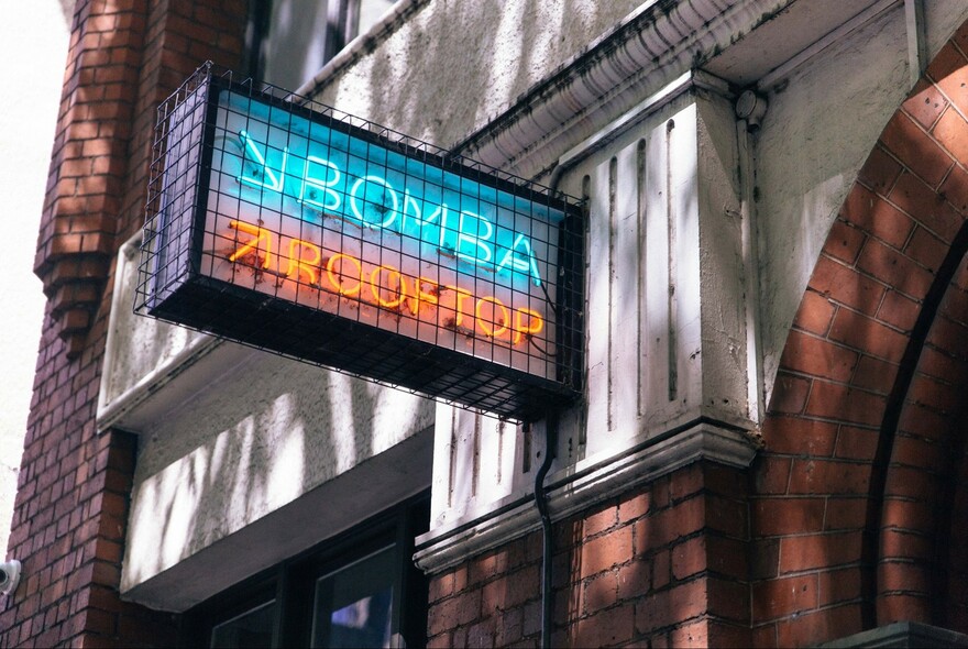 Neon sign with arrows pointing up to rooftop bar and down to Bomba restaurant.