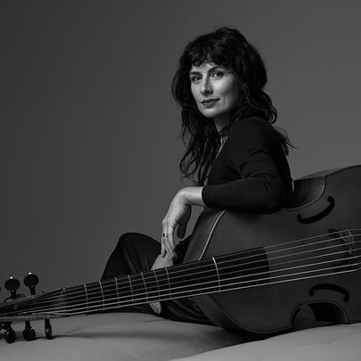 Black and white photo of musican Laura Vaughan sitting on the floor her arm draped over her viola.