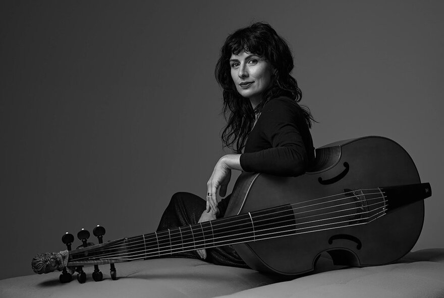 Black and white photo of musican Laura Vaughan sitting on the floor her arm draped over her viola.