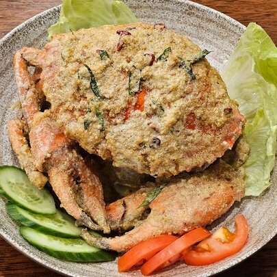 A whole fried crab in a bowl with a few pieces of lettuce, sliced cucumber and tomato.