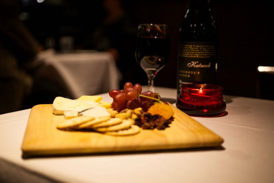 Cheese board platter with a bottle of wine and a glass on a table.