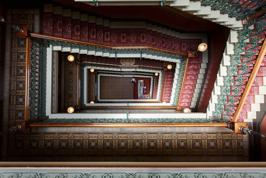 View looking down from the top of the carpeted  staircase at Windsor Hotel onto the ground floor, from at least five or six floors up.