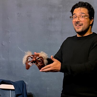 A man in a black long sleeved top holding up a Commedia dell’Arte mask.