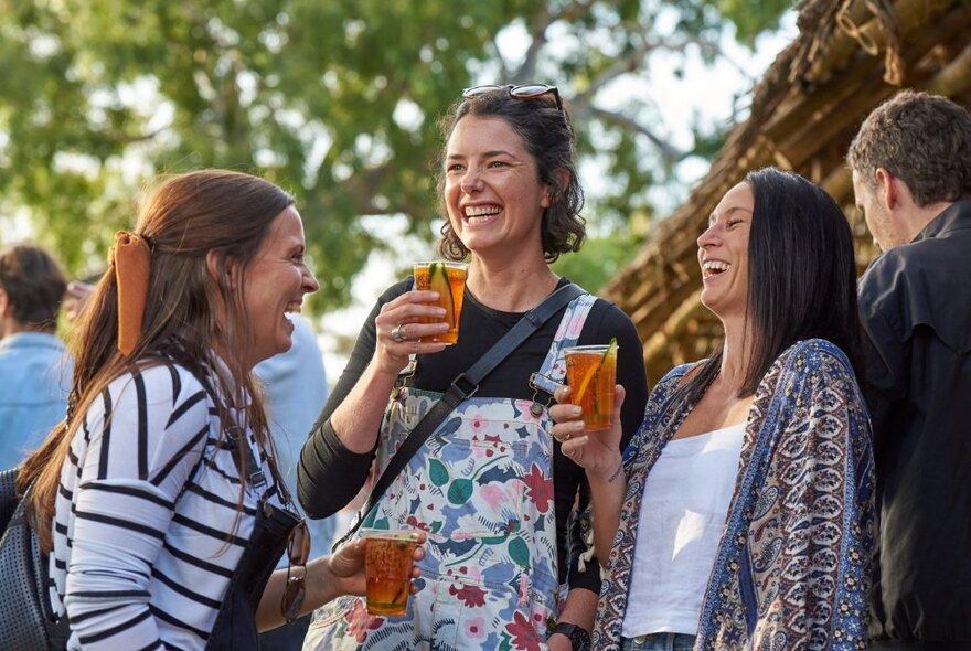 A group of friends laughing and enjoying themselves outdoors, holding drinks in their hands. 