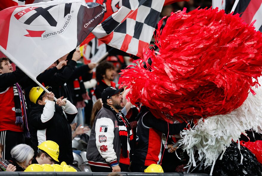 A view of the St Kilda cheer squad at an AFL match, pompoms and flags waving. 