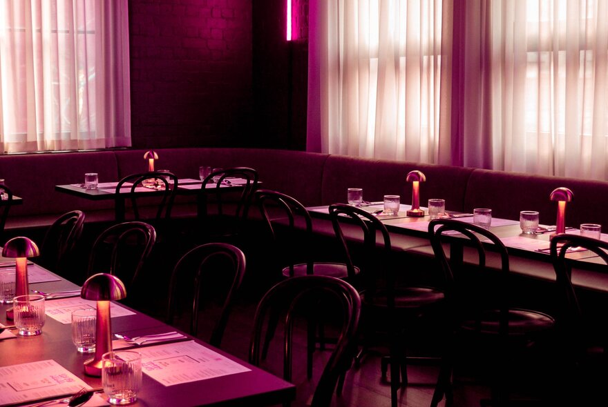 A darkened, empty restaurant space lit up only by a pink neon light.