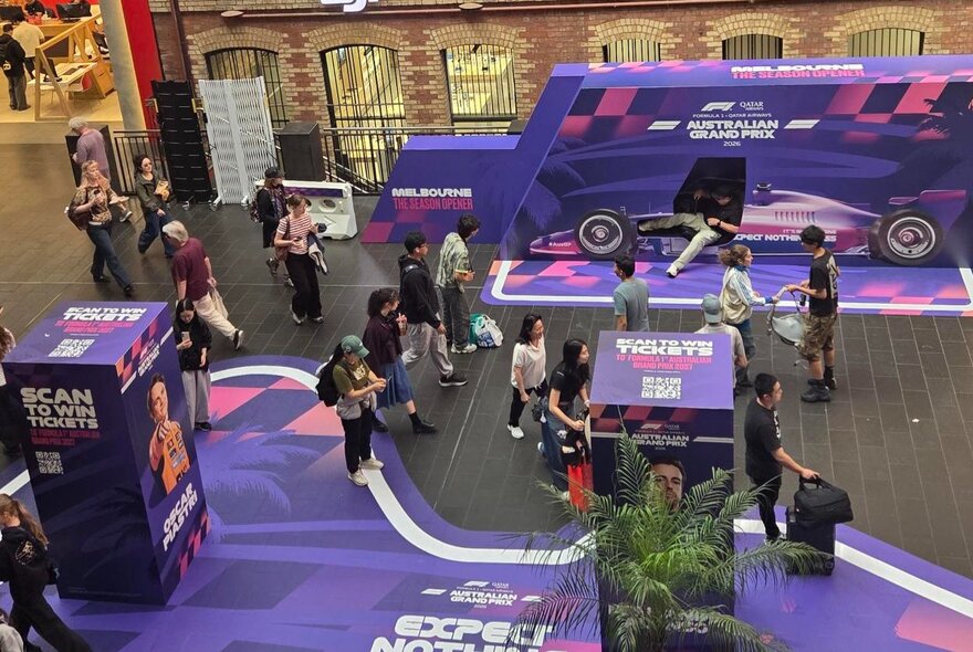 Looking down on people at a pop-up installation within Melbourne Central featuring purple Grand Prix themed graphics. 