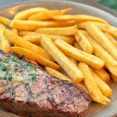 A 300g Black Angus porterhouse steak on a round white plate with chips.