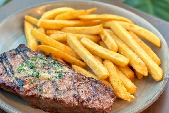 A 300g Black Angus porterhouse steak on a round white plate with chips.
