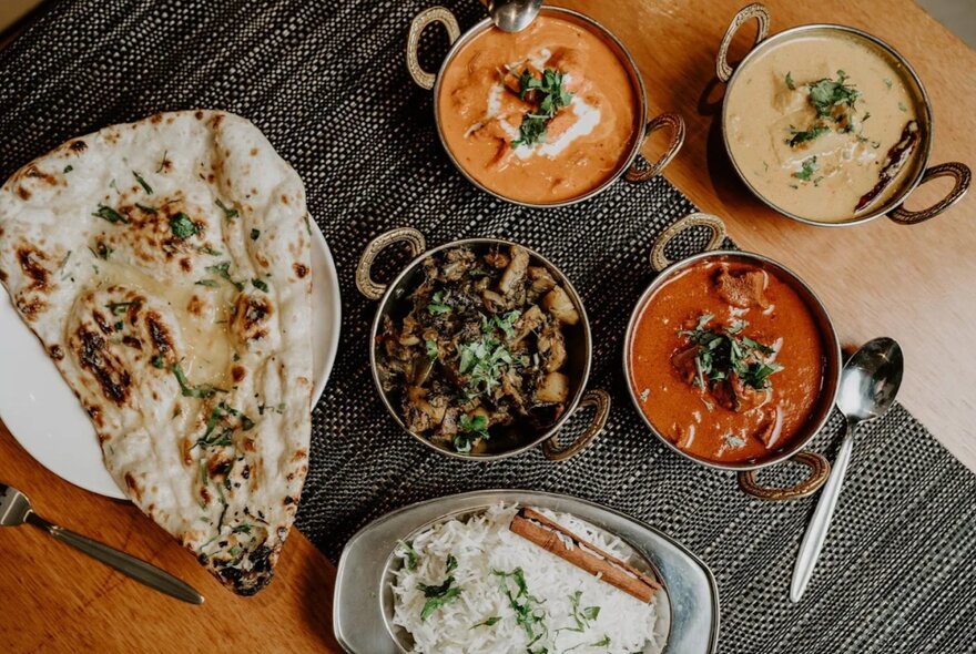 Looking down on a table set with Indian food -curries in bowls and naan bread.
