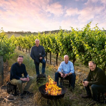 Four winemakers sitting on milk crates around an outdoor fire in the middle of a vineyard.