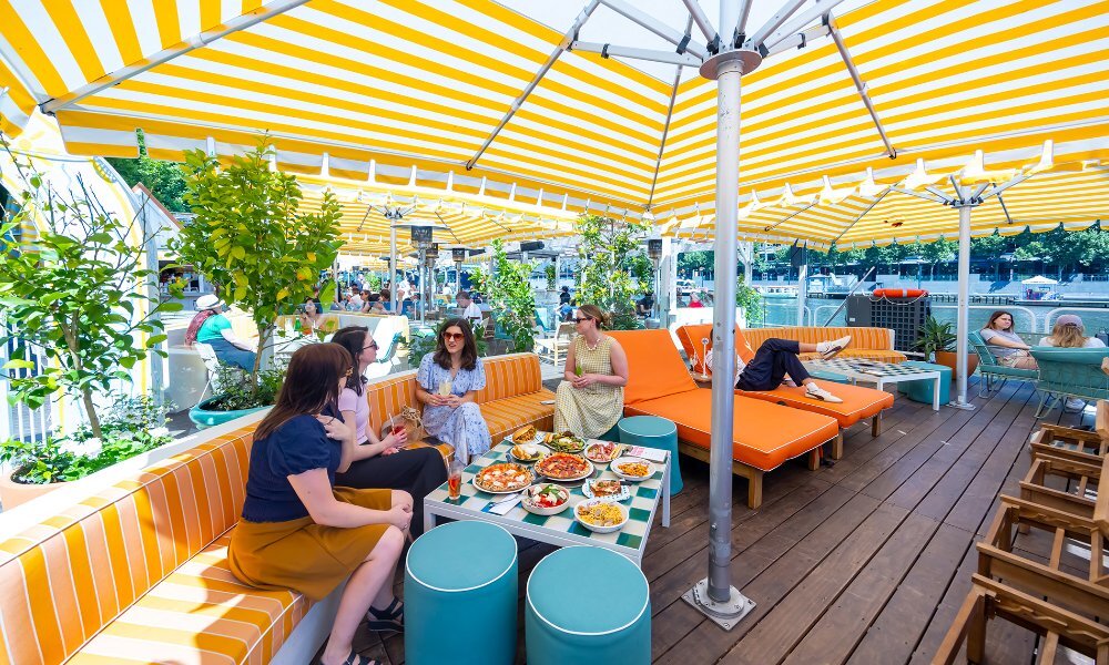 Four friends dining on Italian food in an outdoor bar under a yellow umbrella.