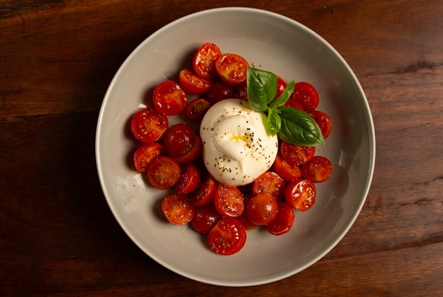 Looking down on a bowl of cherry tomato and burrata and basil. 