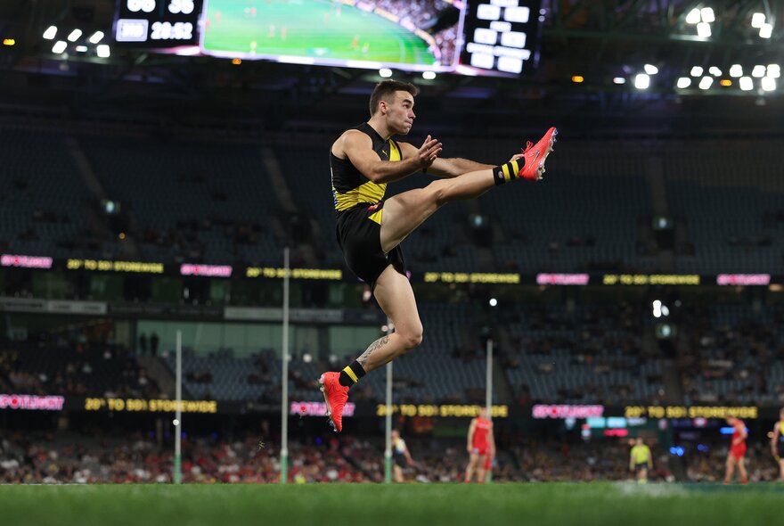 A Richmond player kicking a ball with his leg in the air at a match. 