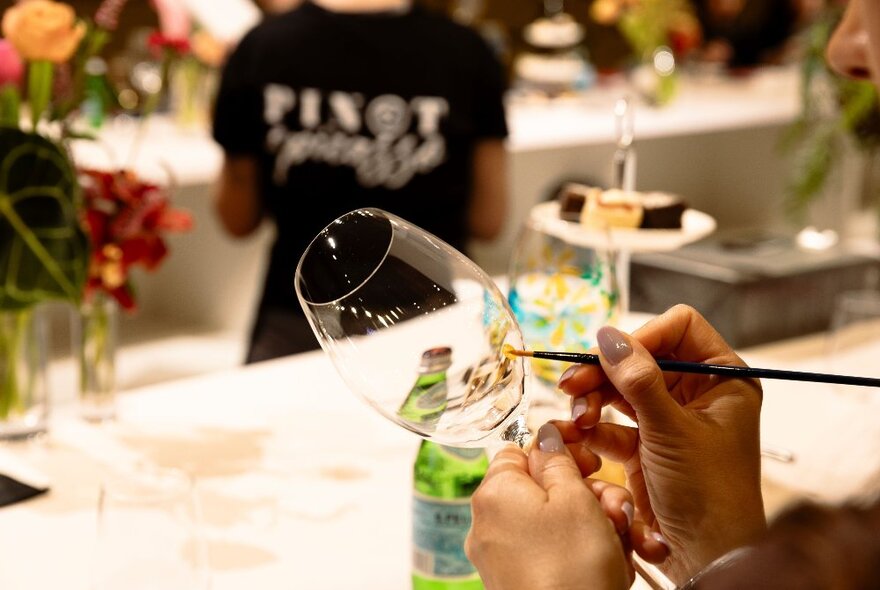 A close-up of someone's hands painting a wine glass. 