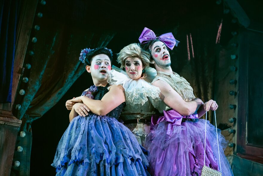 Three chorus figures wearing taffeta Victorian-inspired gowns.