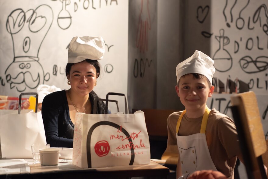 Children wearing chef's hats and aprons with bags of products.