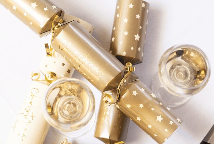 Gold Christmas crackers next to glasses of white wine.