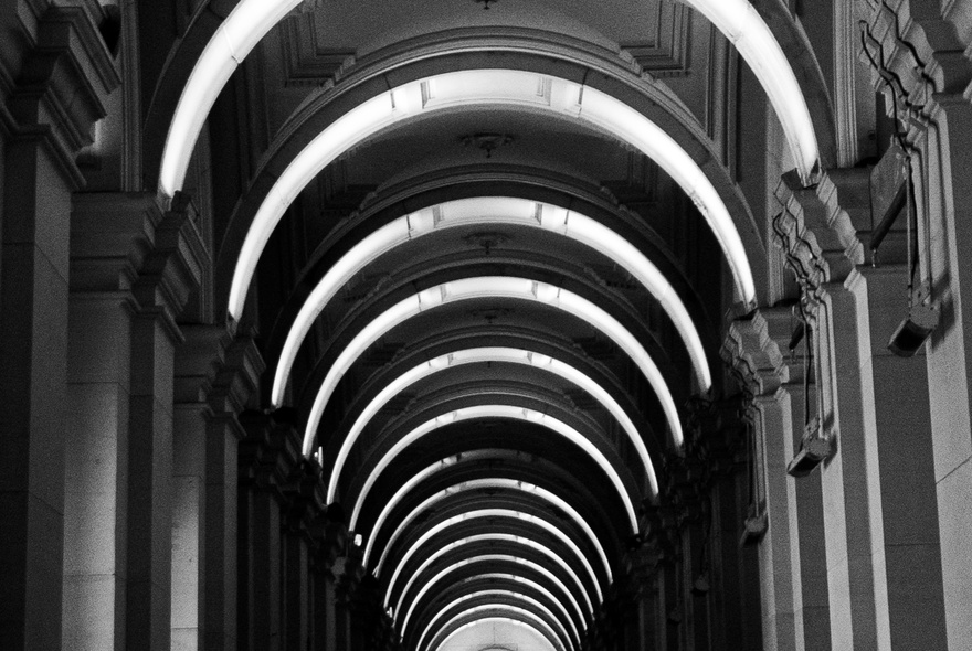 A black and white image of the inside of a building with a vaulted ceiling. 