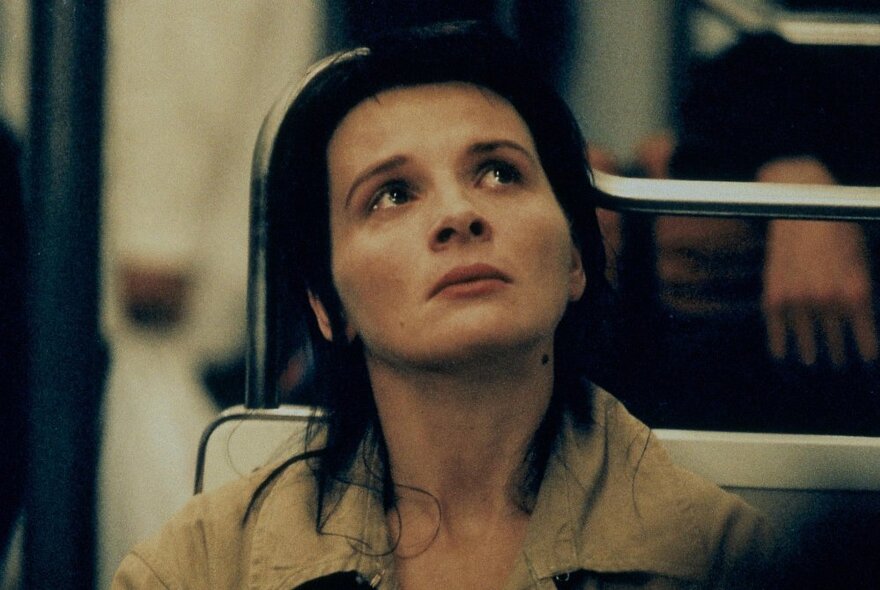 A still image from a film showing actress Juliette Binoche looking up, close to tears, on public transport.