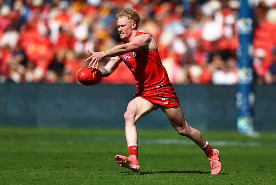 Gold Coast AFL footballer kicking a ball during a game.