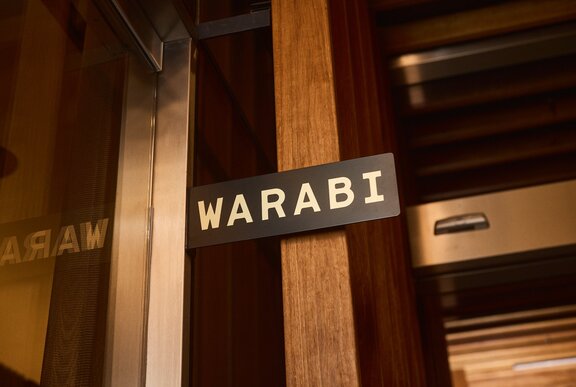 A small, simple sign attached to a wooden post with the restaurant name, Warabi.