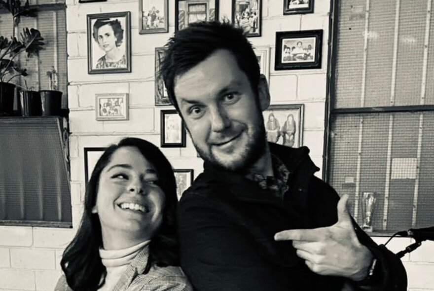Male and female duo posing in front of a wall covered with framed pictures.
