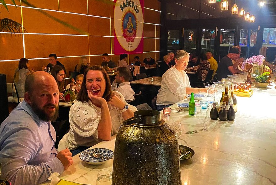People on a long bar table in a full restaurant. 